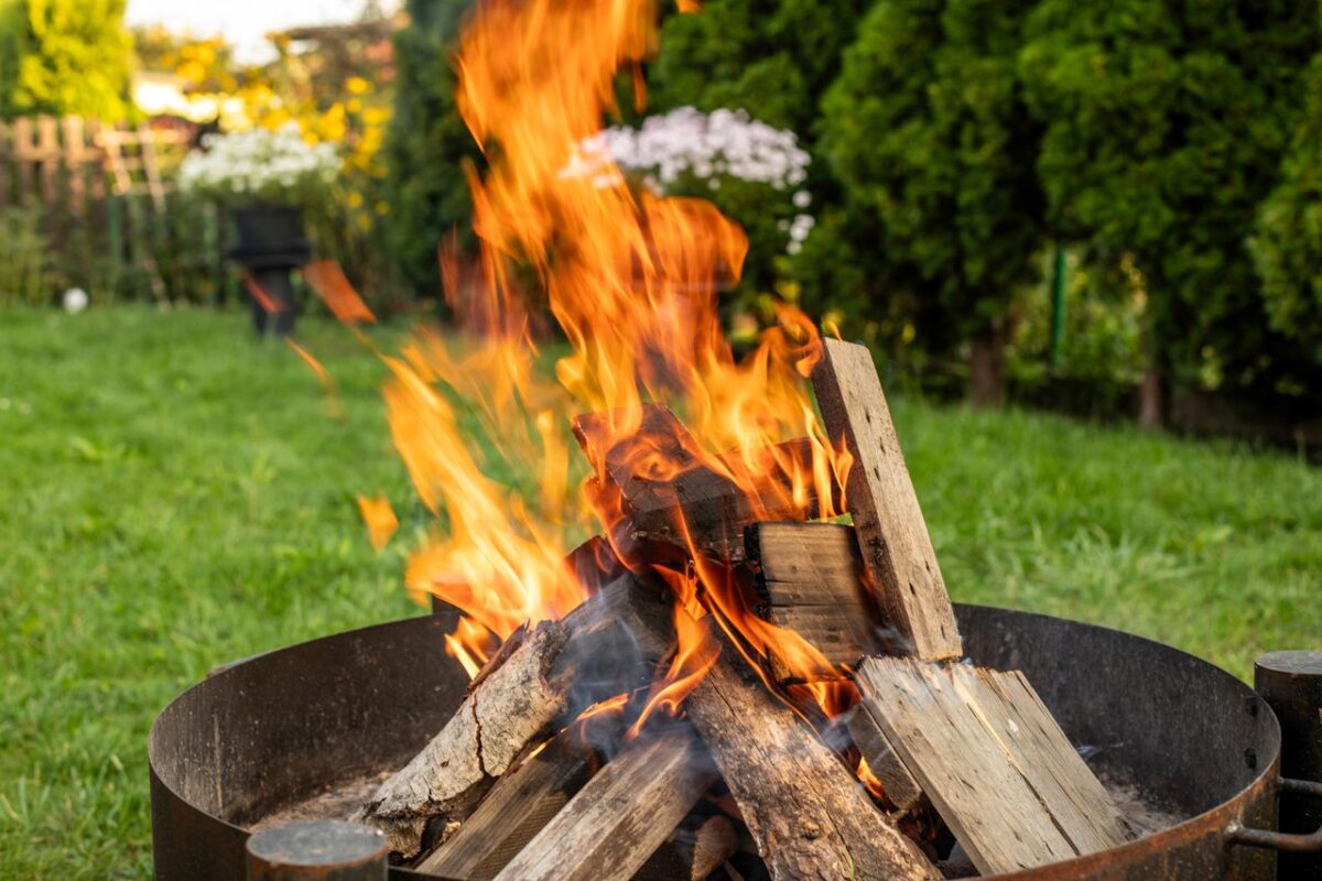 Outdoor corten steel fire pit with burning wood in a garden setting