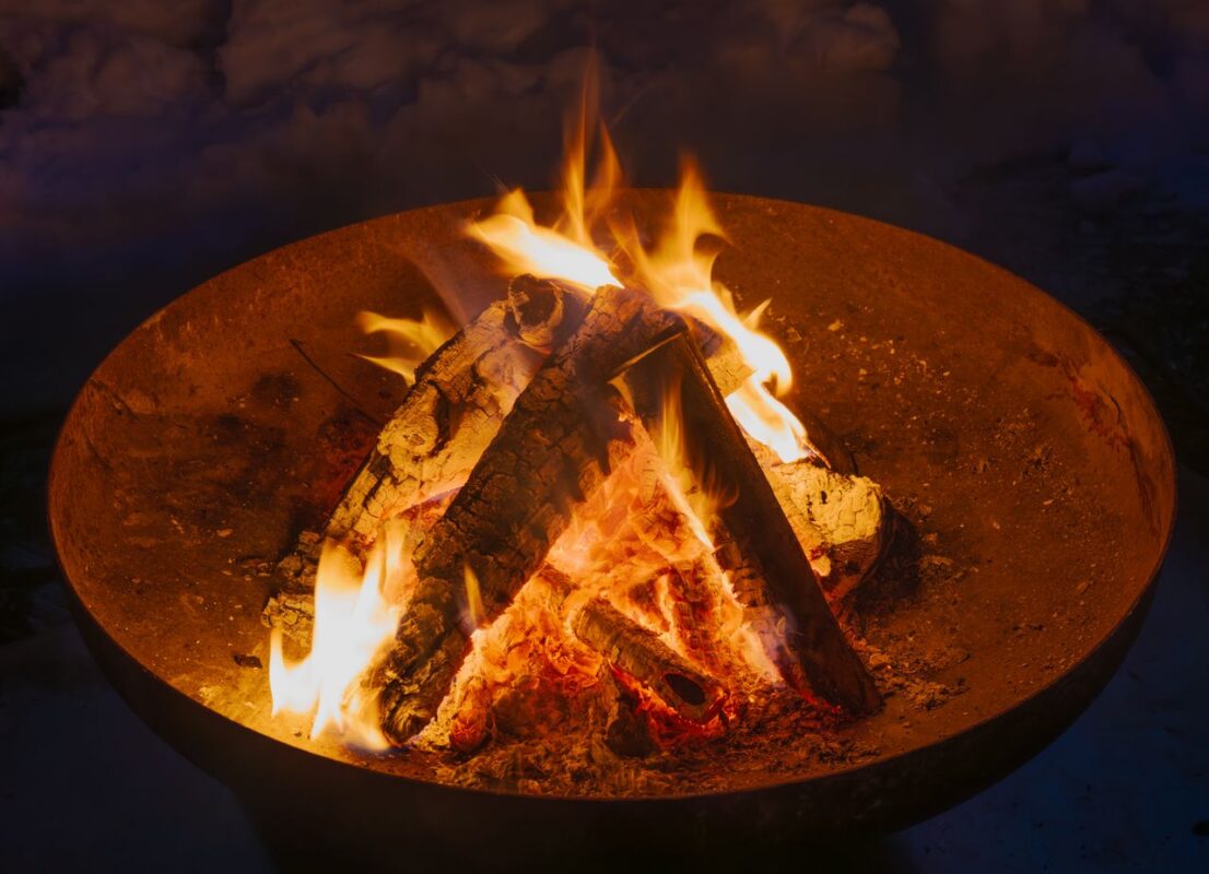 Outdoor corten steel fire pit with burning wood in a garden setting