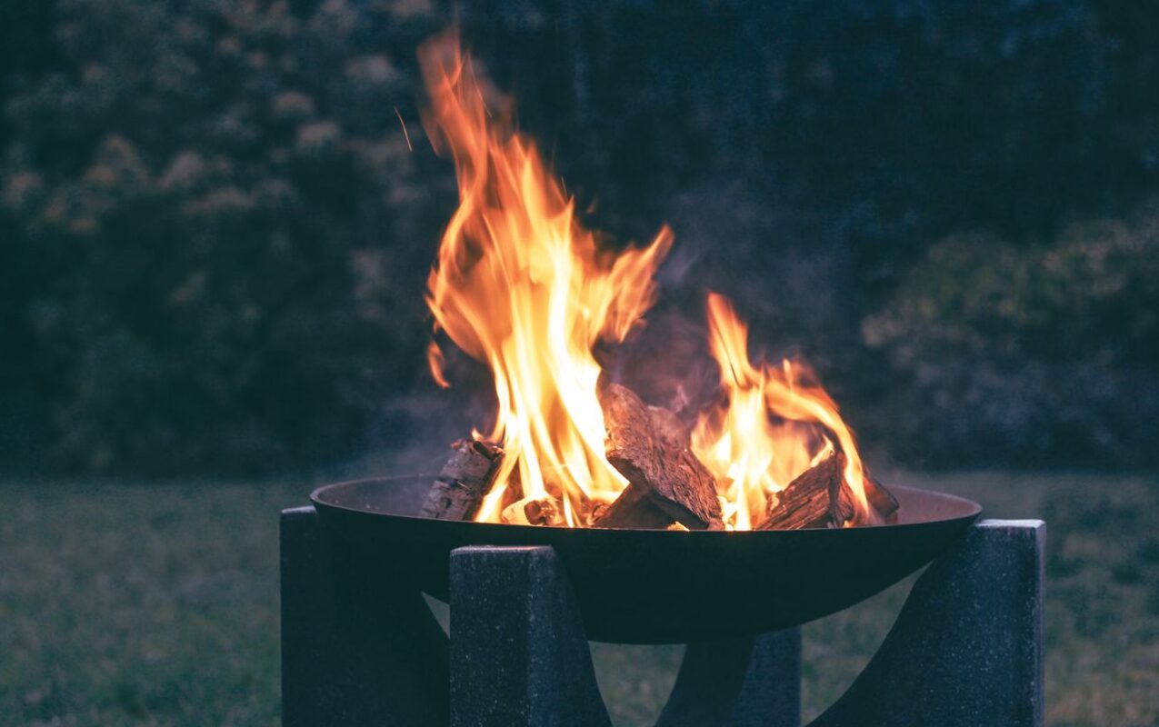 Outdoor corten steel fire pit with burning wood in a garden setting