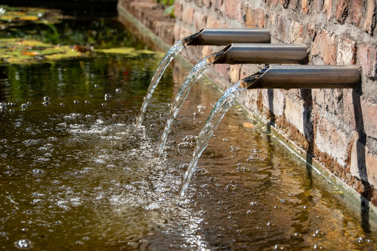 Corten steel water feature with metal spouts in a landscaped garden